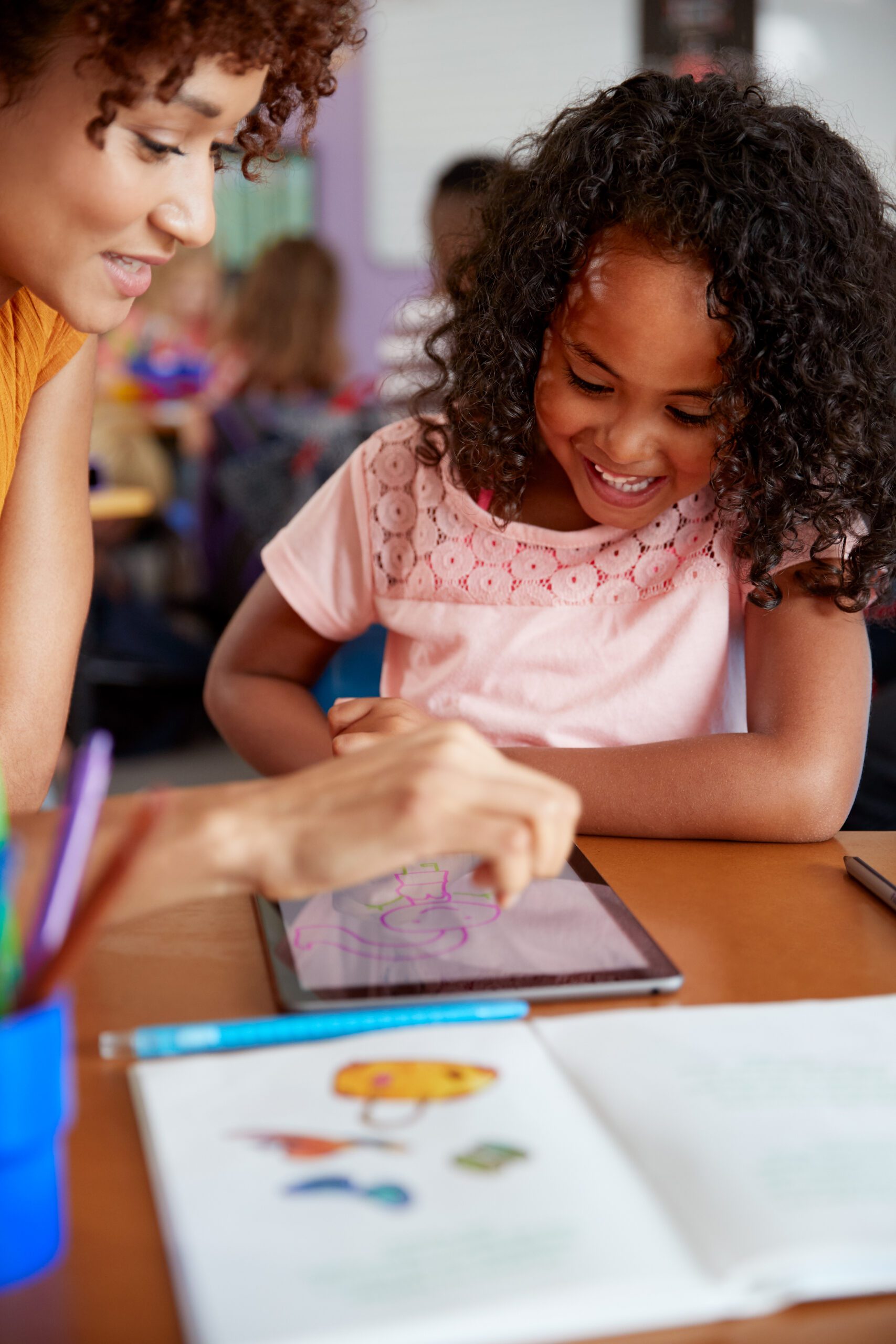 Elementary School Teacher And Female Pupil Drawing Using Digital Tablet In Classroom Teacher and student drawing on a digital tablet in a classroom